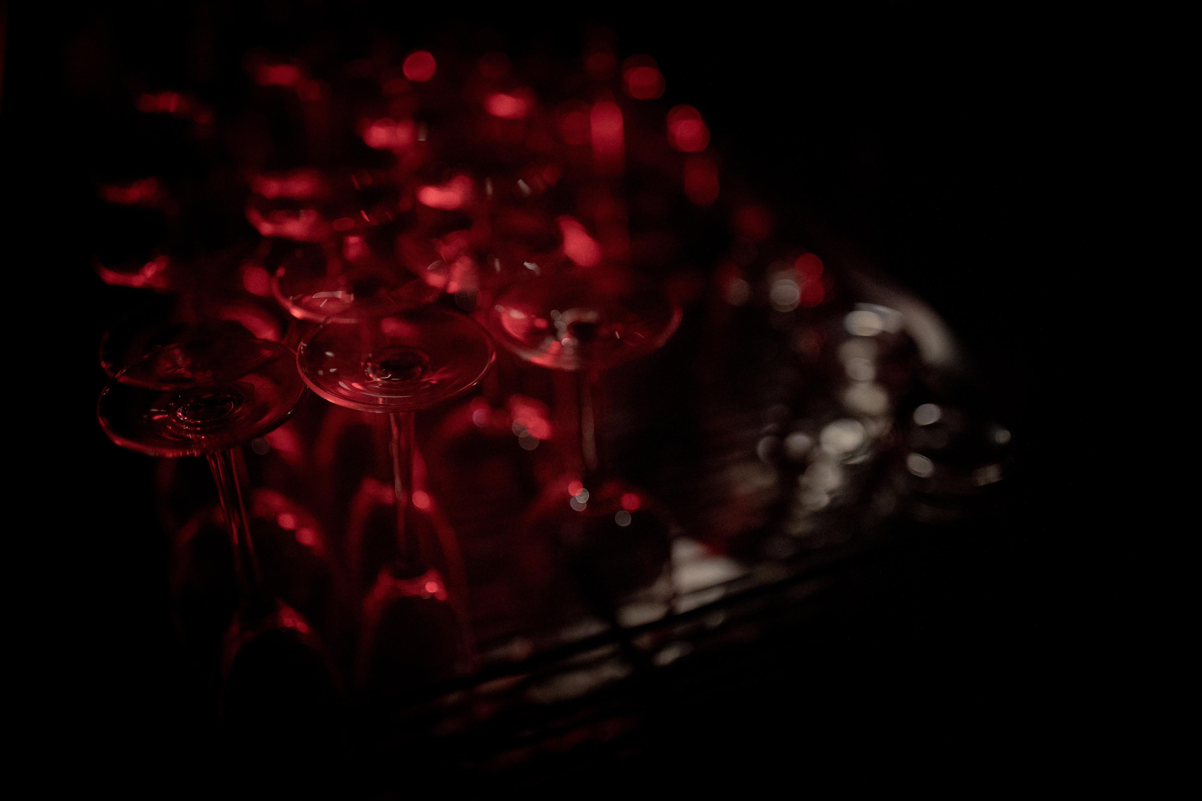 Several wine glasses in the dark, red light illuminating their sides.