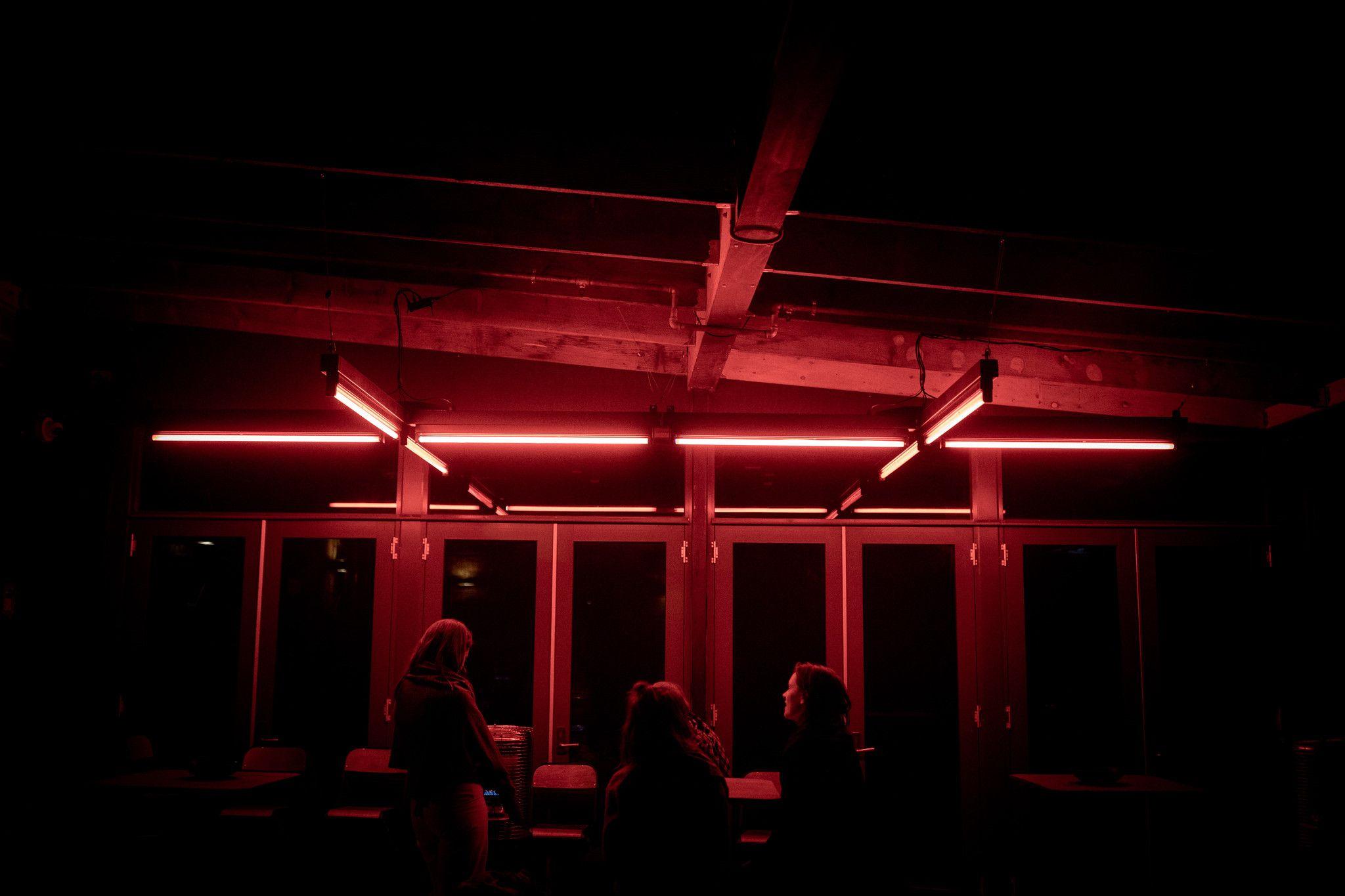 Friends gathered around an outdoor table illuminated in red light by a large hanging double cross