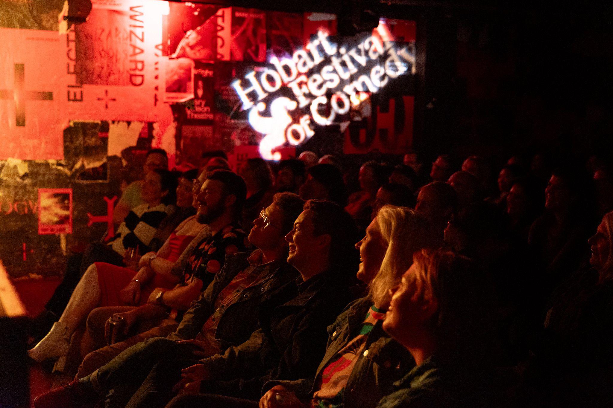 A seated audience laughs at a comedy act out of frame