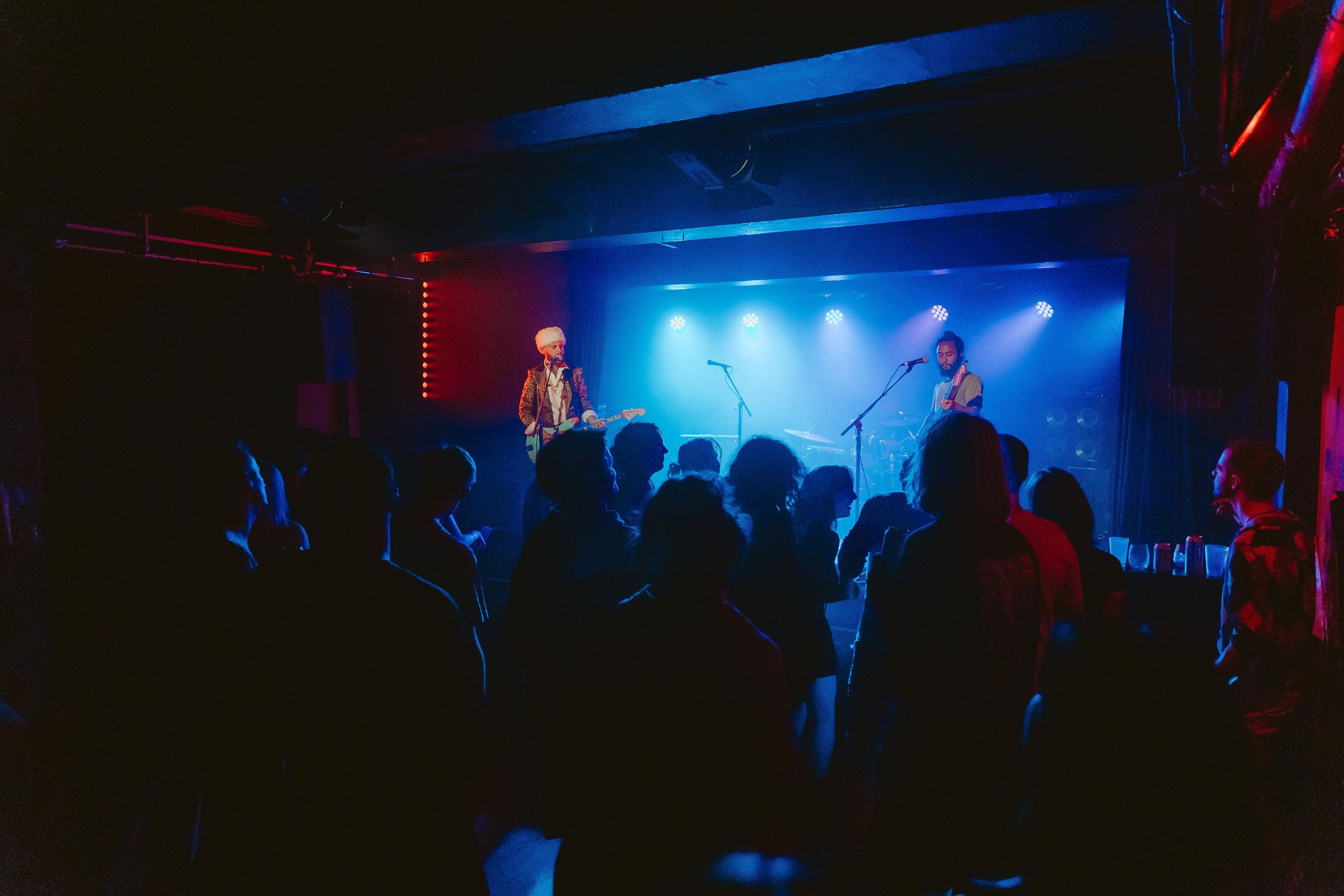 A band performs on-stage, several blue lights illuminate the stage behind them.