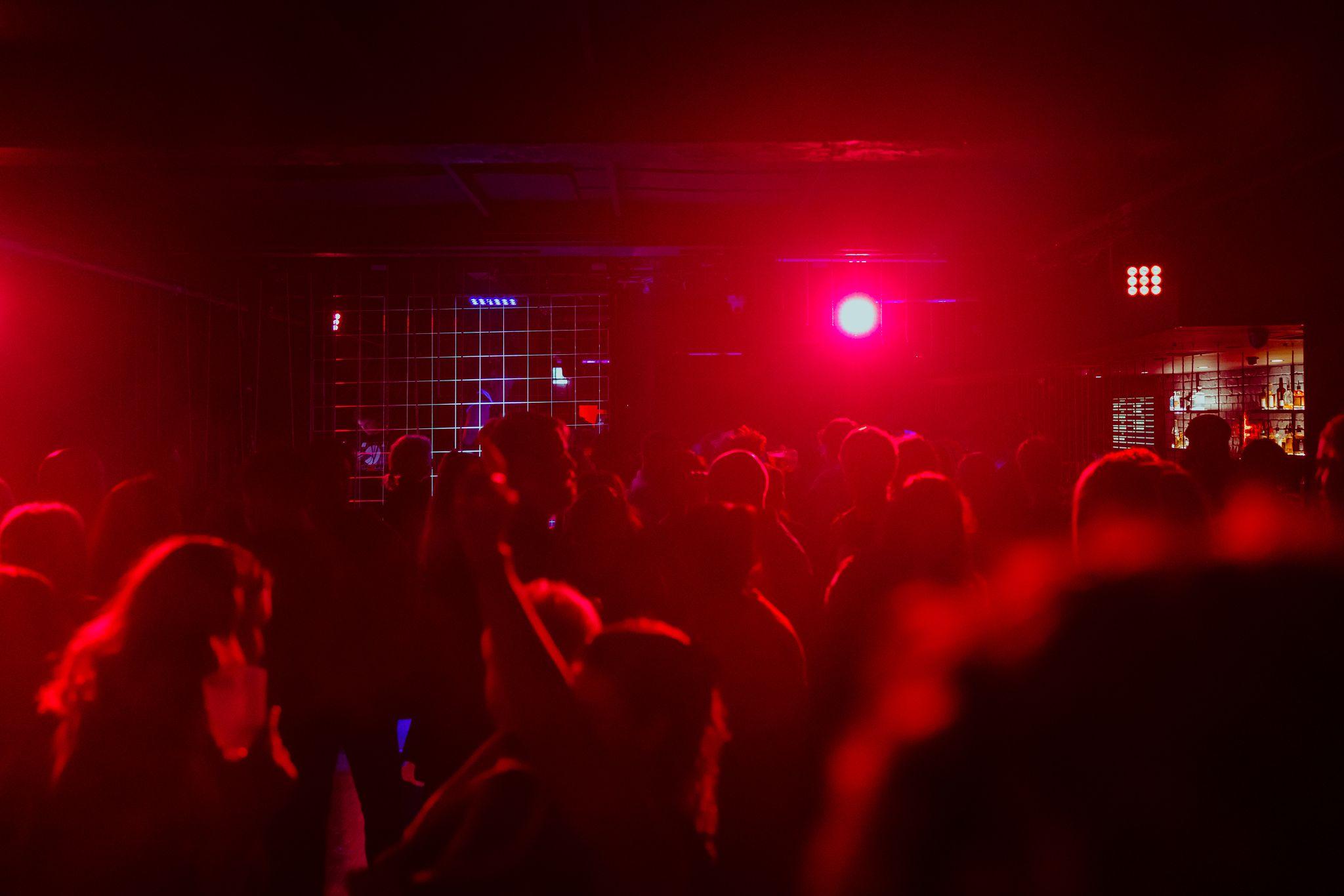 Revellers dance bathed in red light as a DJ gets down to work in a neon green cage